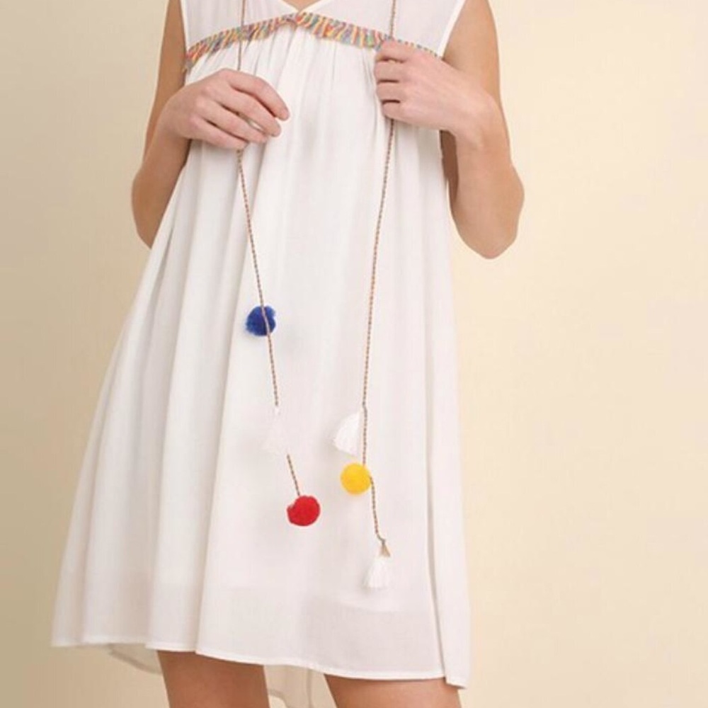 White, flowy dress with colored pom poms.